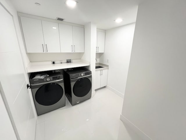 washroom with light tile patterned flooring, washer and clothes dryer, cabinets, and sink