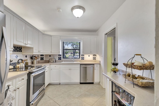 kitchen with appliances with stainless steel finishes, white cabinets, light tile patterned floors, and sink