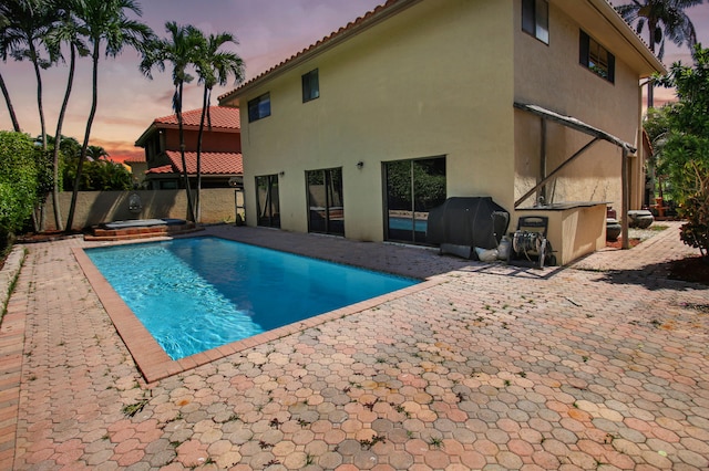 pool at dusk with an in ground hot tub and a patio