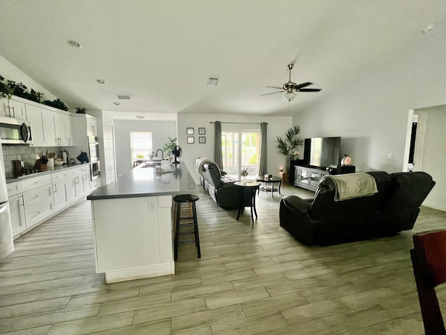 kitchen featuring ceiling fan, lofted ceiling, tasteful backsplash, and white cabinets