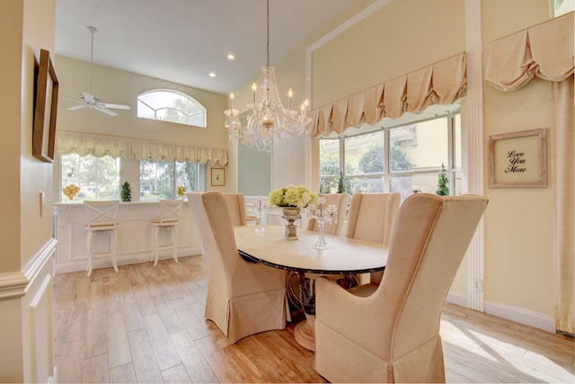 dining room with a high ceiling, ceiling fan with notable chandelier, light hardwood / wood-style flooring, and plenty of natural light