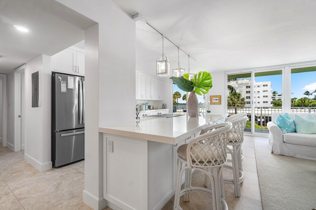 kitchen featuring pendant lighting, stainless steel fridge, white cabinets, a kitchen bar, and kitchen peninsula