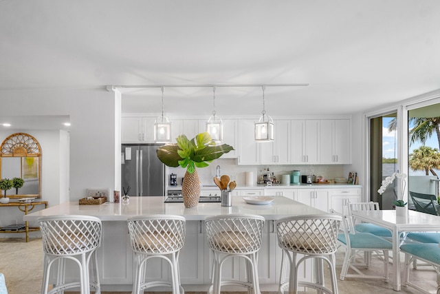 kitchen featuring tasteful backsplash, white cabinets, fridge, a kitchen breakfast bar, and decorative light fixtures