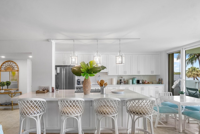 kitchen featuring a kitchen bar, hanging light fixtures, stainless steel refrigerator, decorative backsplash, and white cabinets