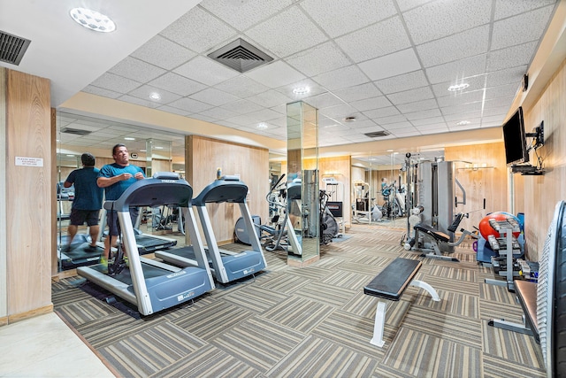 workout area featuring carpet, a drop ceiling, and wood walls