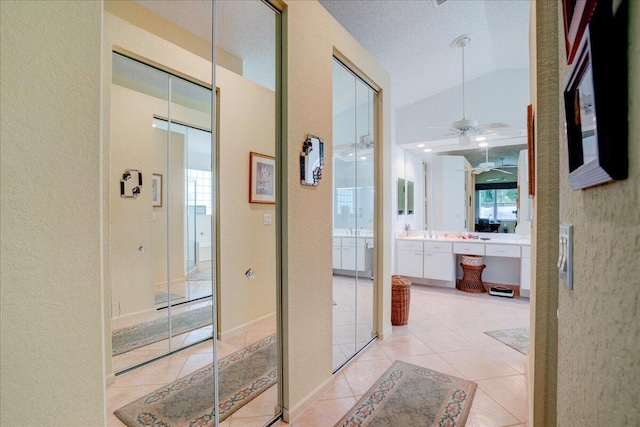 hall with a textured ceiling, lofted ceiling, and light tile patterned floors