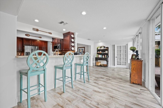 kitchen featuring light hardwood / wood-style floors, a textured ceiling, appliances with stainless steel finishes, and kitchen peninsula