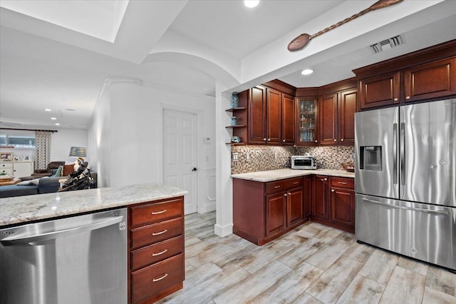 kitchen featuring appliances with stainless steel finishes, light hardwood / wood-style flooring, light stone counters, backsplash, and a skylight