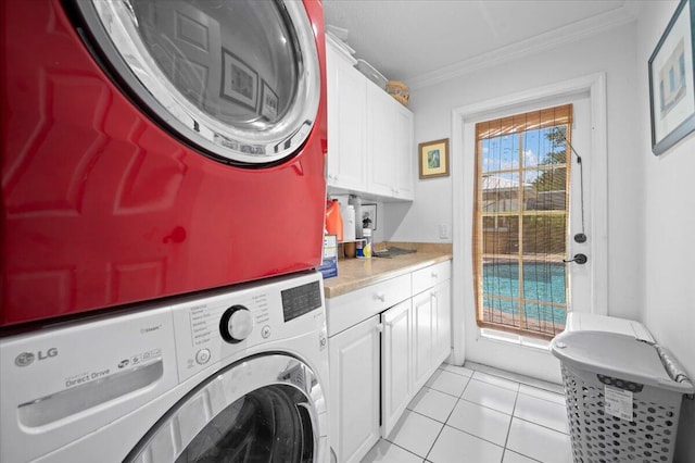 laundry room with cabinets, crown molding, light tile patterned floors, and stacked washing maching and dryer