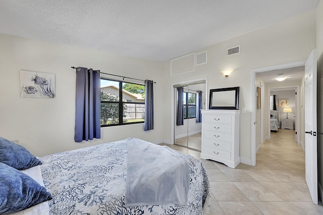 bedroom featuring a closet, visible vents, a textured ceiling, and light tile patterned floors