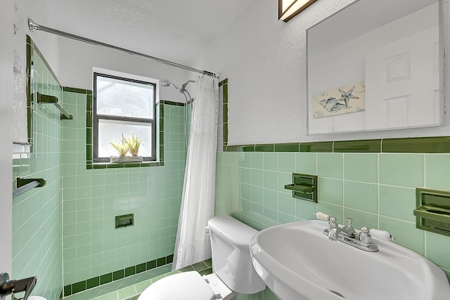 full bathroom with a wainscoted wall, tile walls, toilet, a sink, and a tile shower