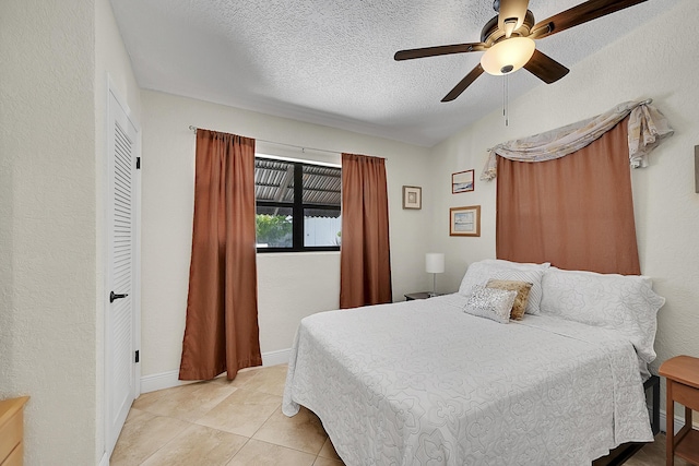 bedroom with a ceiling fan, a textured ceiling, baseboards, and light tile patterned floors