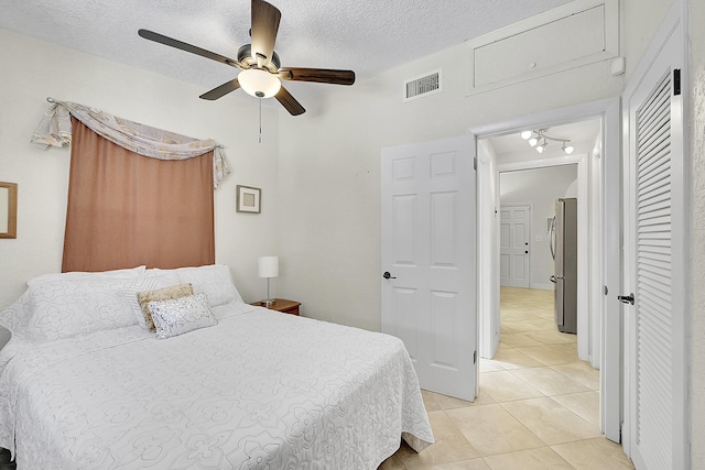 bedroom with light tile patterned floors, visible vents, a textured ceiling, and freestanding refrigerator