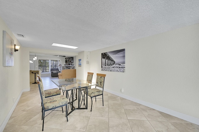 dining room with a textured ceiling, light tile patterned flooring, a skylight, visible vents, and baseboards