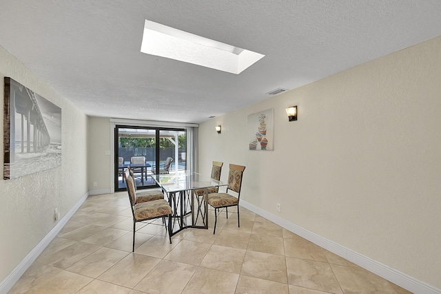 dining area featuring a skylight, light tile patterned floors, visible vents, and a textured ceiling