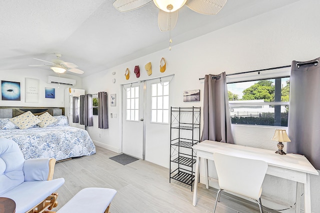 bedroom with a wall unit AC, lofted ceiling, light wood-style flooring, ceiling fan, and a textured ceiling