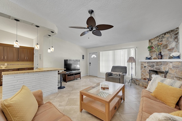 living room with a textured ceiling, vaulted ceiling, a stone fireplace, and light tile patterned flooring