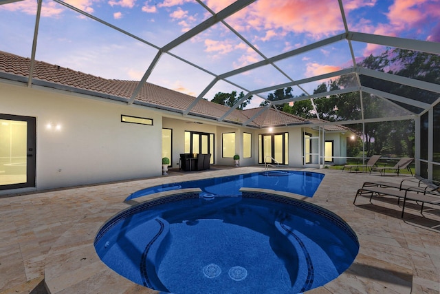 pool at dusk with glass enclosure, a pool with connected hot tub, ceiling fan, and a patio area