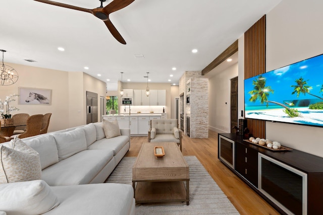 living room with ceiling fan with notable chandelier, sink, and light wood-type flooring