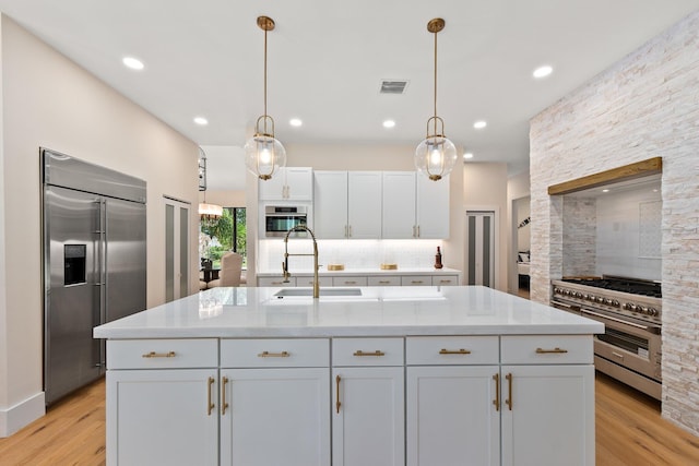 kitchen with pendant lighting, exhaust hood, a center island with sink, light hardwood / wood-style floors, and high quality appliances