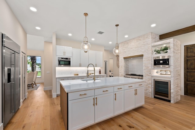 kitchen featuring white cabinets, sink, light hardwood / wood-style floors, appliances with stainless steel finishes, and a kitchen island with sink