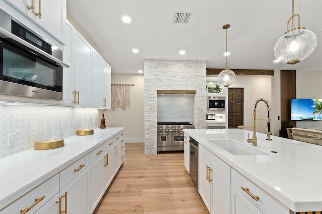 kitchen with stainless steel appliances, sink, light hardwood / wood-style floors, decorative backsplash, and an island with sink