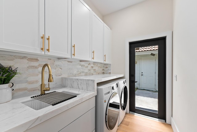 clothes washing area featuring washer and clothes dryer, sink, cabinets, and light hardwood / wood-style floors