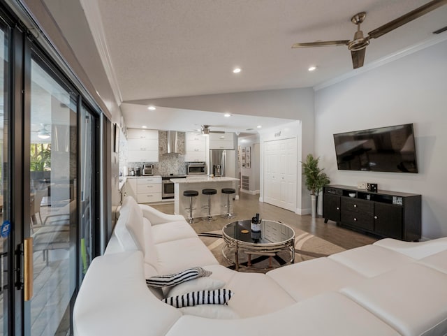 living room featuring wood-type flooring, ceiling fan, ornamental molding, vaulted ceiling, and a textured ceiling