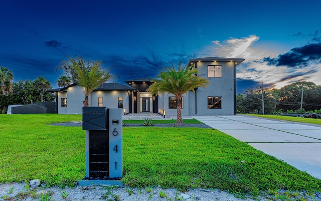 contemporary house with a front yard, fence, driveway, and stucco siding