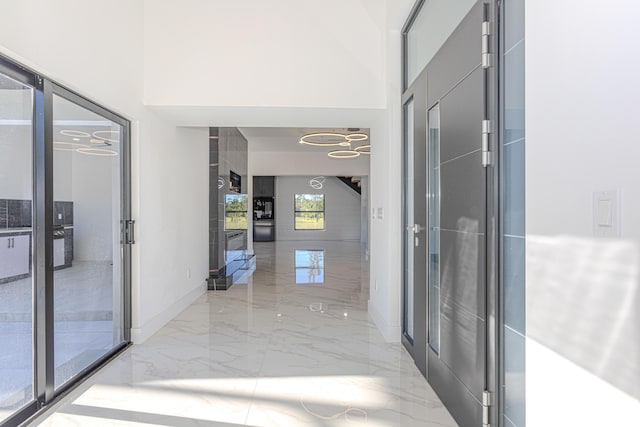 corridor featuring marble finish floor, a high ceiling, and baseboards