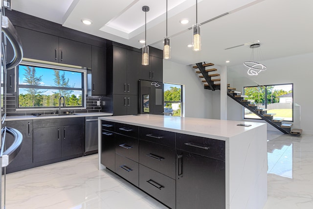 kitchen with marble finish floor, decorative light fixtures, a kitchen island, a sink, and dark cabinets