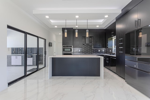 kitchen with light countertops, dark cabinetry, wall chimney exhaust hood, a tray ceiling, and pendant lighting