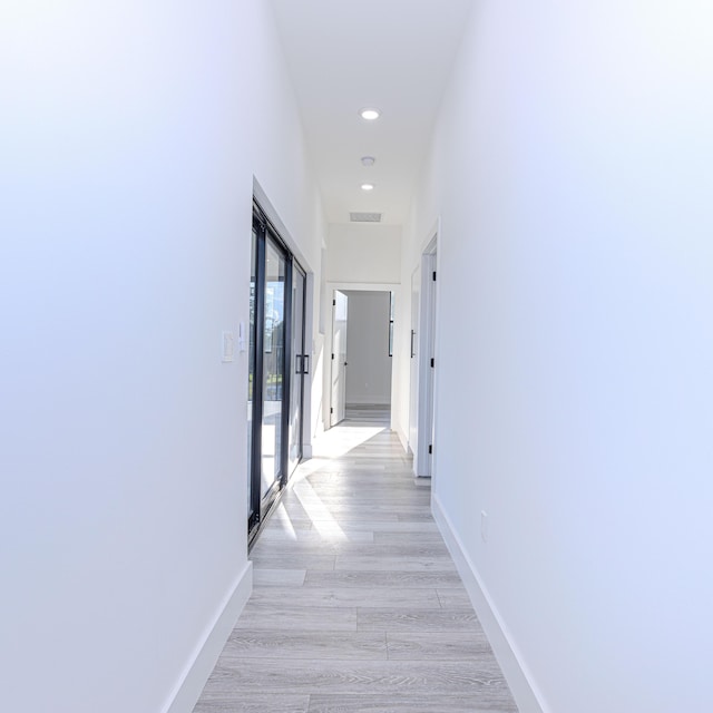 corridor with light wood finished floors, recessed lighting, visible vents, and baseboards