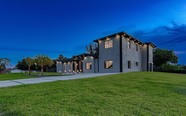 back of property featuring a lawn, driveway, and stucco siding