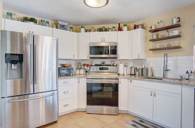 kitchen with white cabinetry, light stone countertops, stainless steel appliances, and backsplash