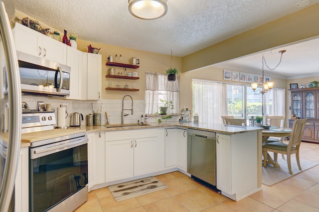 kitchen with light tile patterned floors, kitchen peninsula, stainless steel appliances, light stone countertops, and sink