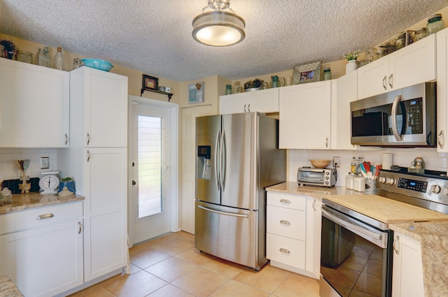 kitchen with a textured ceiling, white cabinets, light stone counters, stainless steel appliances, and decorative backsplash