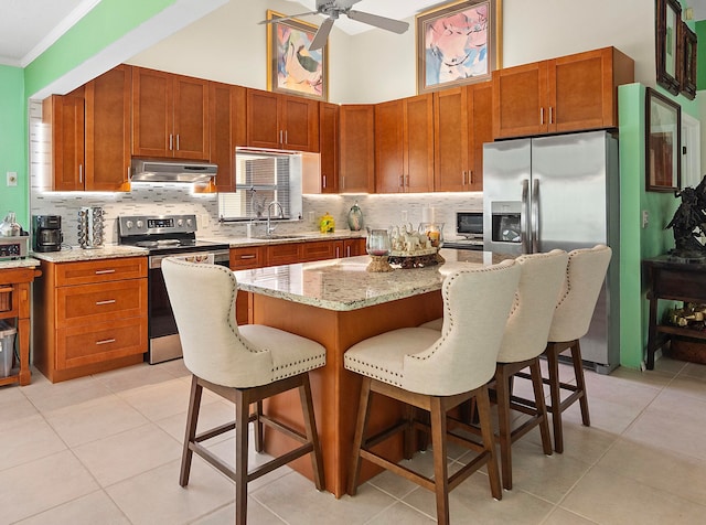 kitchen with appliances with stainless steel finishes, backsplash, light tile patterned floors, a center island, and ceiling fan