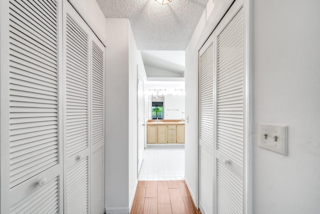 corridor with lofted ceiling, wood-type flooring, and a textured ceiling