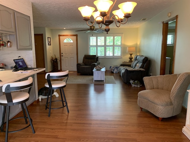 living room with ceiling fan with notable chandelier, dark hardwood / wood-style floors, and a textured ceiling