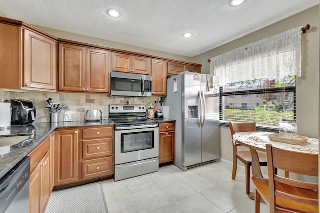 kitchen featuring tasteful backsplash, stainless steel appliances, light tile patterned floors, a textured ceiling, and dark stone countertops