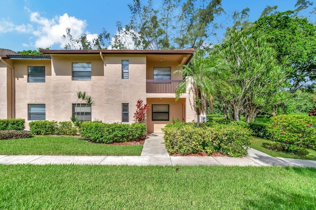 multi unit property with a balcony, a front yard, and stucco siding