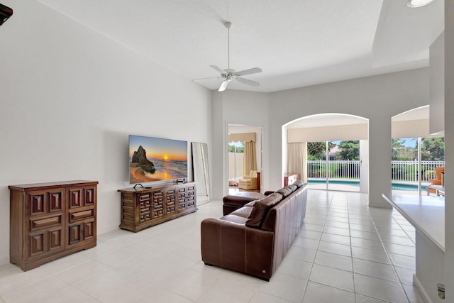 living area with a ceiling fan, arched walkways, and light tile patterned floors