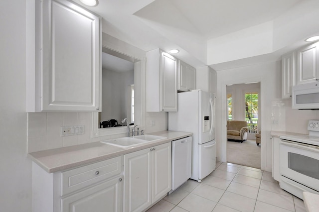 kitchen with white cabinets, a sink, light colored carpet, white appliances, and light tile patterned floors