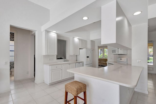 kitchen featuring light tile patterned flooring, white appliances, light countertops, a kitchen bar, and a peninsula