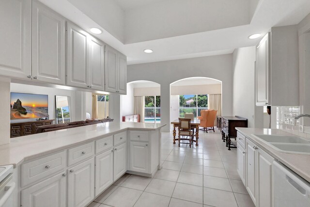 kitchen with white dishwasher, kitchen peninsula, sink, and white cabinets