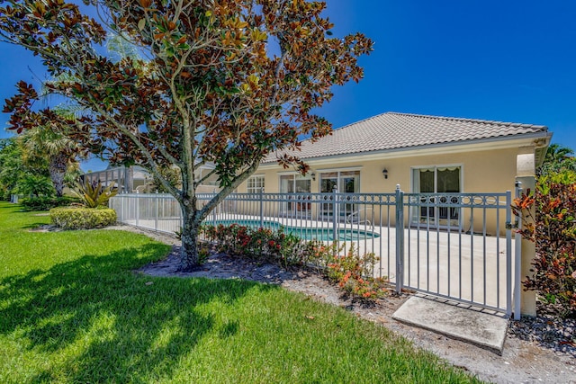 rear view of house featuring a lawn, a tiled roof, fence, a fenced in pool, and stucco siding