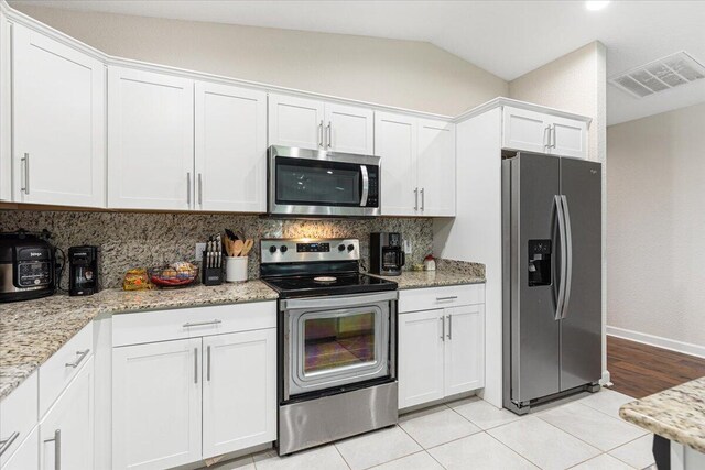 kitchen featuring tasteful backsplash, stainless steel appliances, vaulted ceiling, and light tile patterned floors