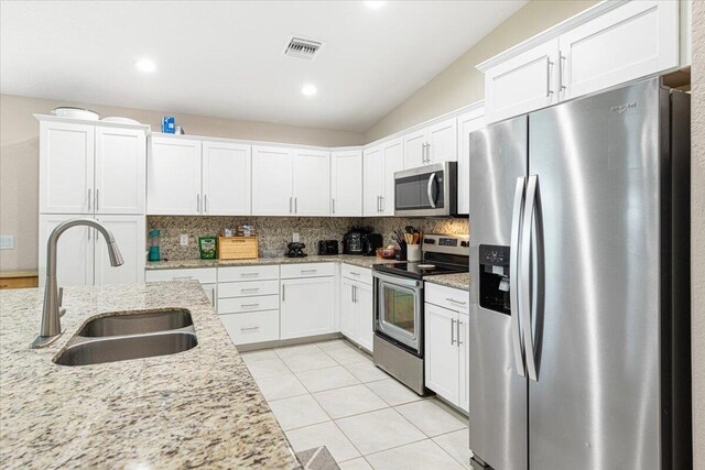 kitchen featuring tasteful backsplash, white cabinets, stainless steel appliances, light stone countertops, and sink