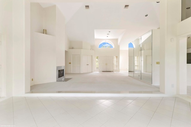 empty room with a tile fireplace, light tile patterned floors, and a towering ceiling